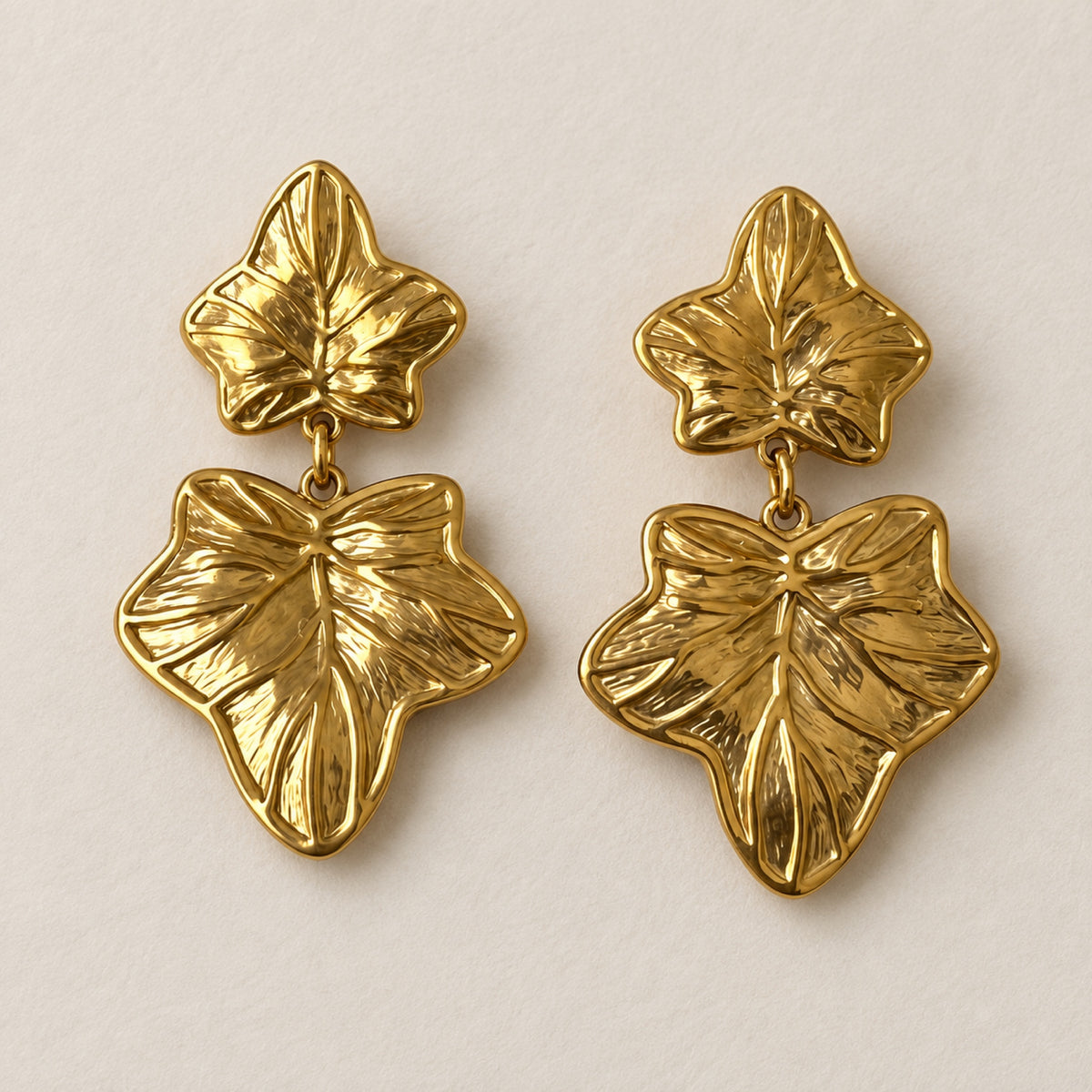Aretes dorados de doble hoja con nervaduras en relieve y diseño colgante. Un detalle de inspiración botánica para complementar tus looks y celebraciones.