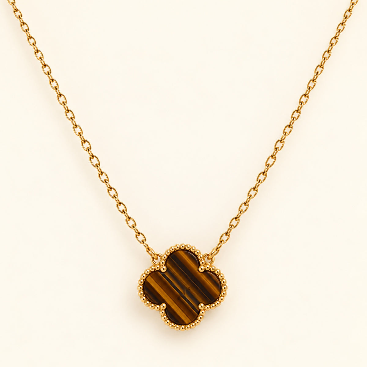 Collar dorado con trébol de cuatro hojas en tonos café y dorados, franjas diagonales y borde de pequeñas cuentas.