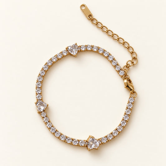 Pulsera tennis dorada con zirconias redondas, tres zirconias en forma de corazón, cierre de mosquetón y cadena de extensión.