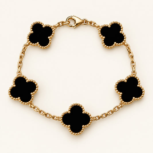 Pulsera con cinco tréboles negros de cuatro hojas, bordes de bolitas y cadena en tono dorado, con cierre tipo langosta sobre fondo marfil.