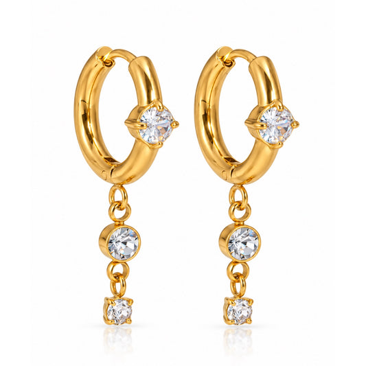 Par de aretes de argolla en tono dorado, cada uno con una zirconia frontal y dos zirconias redondas colgantes, sobre fondo blanco.