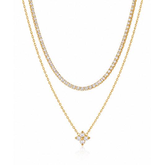 Collar de doble capa en tono dorado con una fila de zirconias y una cadena fina con dije de flor de cuatro pétalos, sobre fondo blanco.